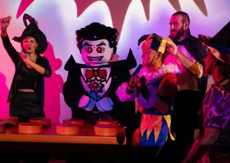 Dracula lego character danging by lego dj deck with kids gethered around wearing halloween costumes.